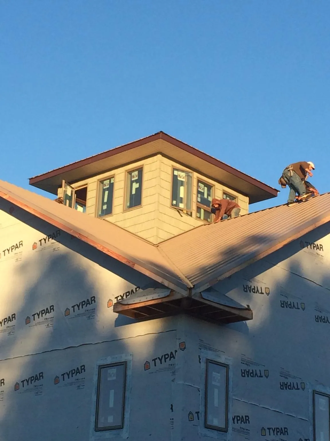 Roofers working around a rooftop cupola on a new metal roof at sunset in Meriden
